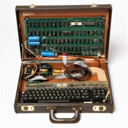 An open briefcase. The top half houses an Apple I circuit board, wired up to a keyboard in the bottom half.