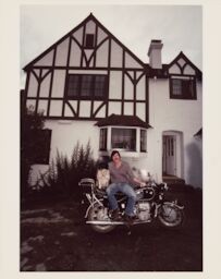 Parked outside his Tudor-style home, Steve shares the seat of his BMW motorcycle with a black and white dog.