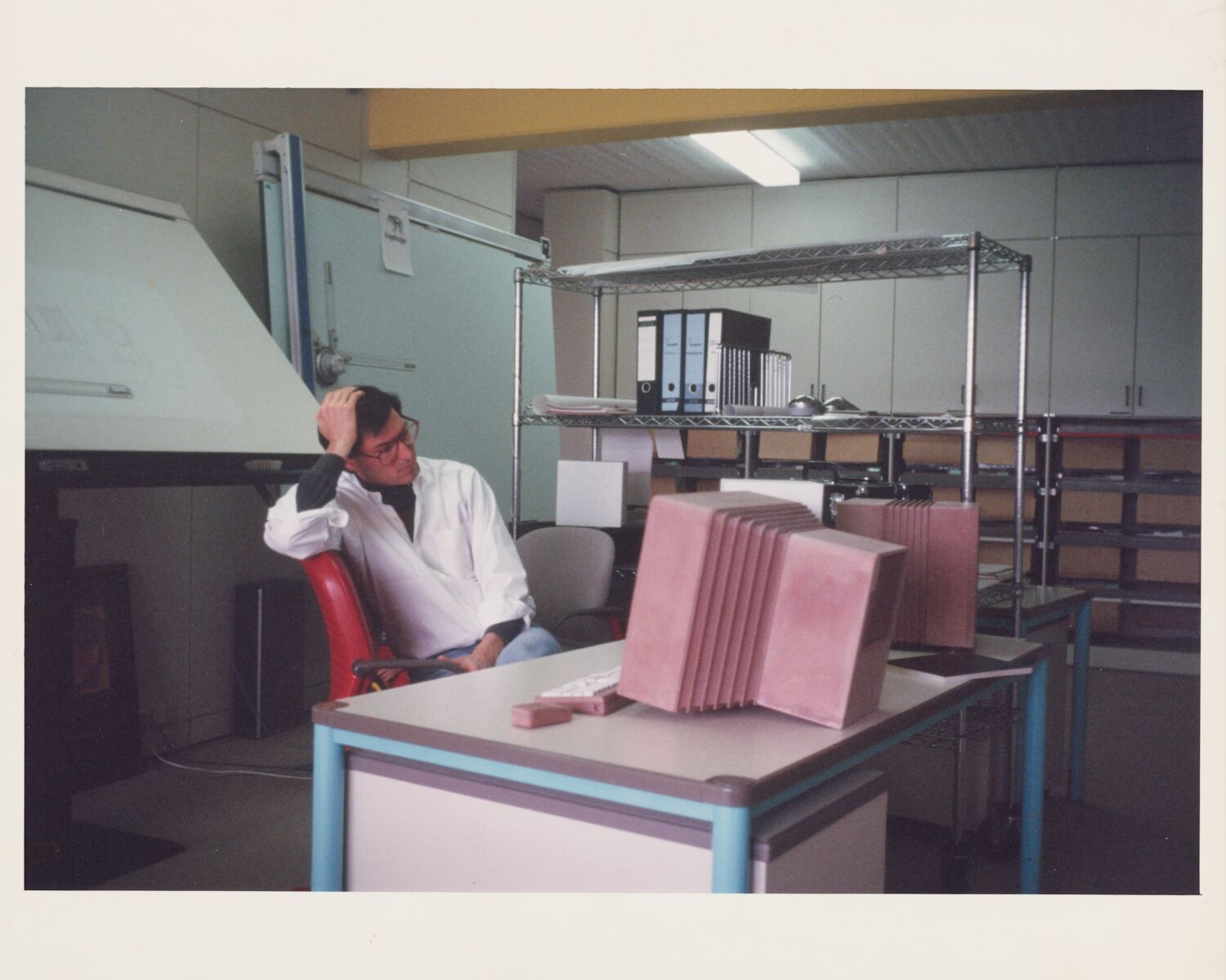 Steve sits in a chair, hand cradling his head, and stares at a life-size pink foam NeXT computer prototype.