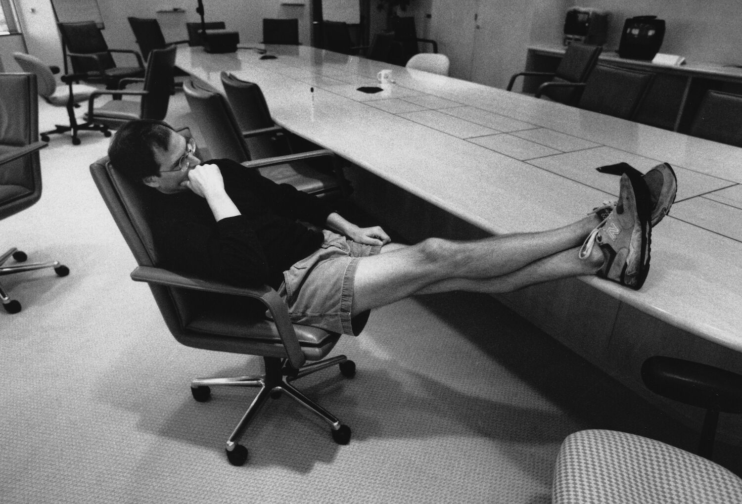 Steve leans back on his chair in a conference room. He is wearing shorts, legs stretched out and feet on the table.