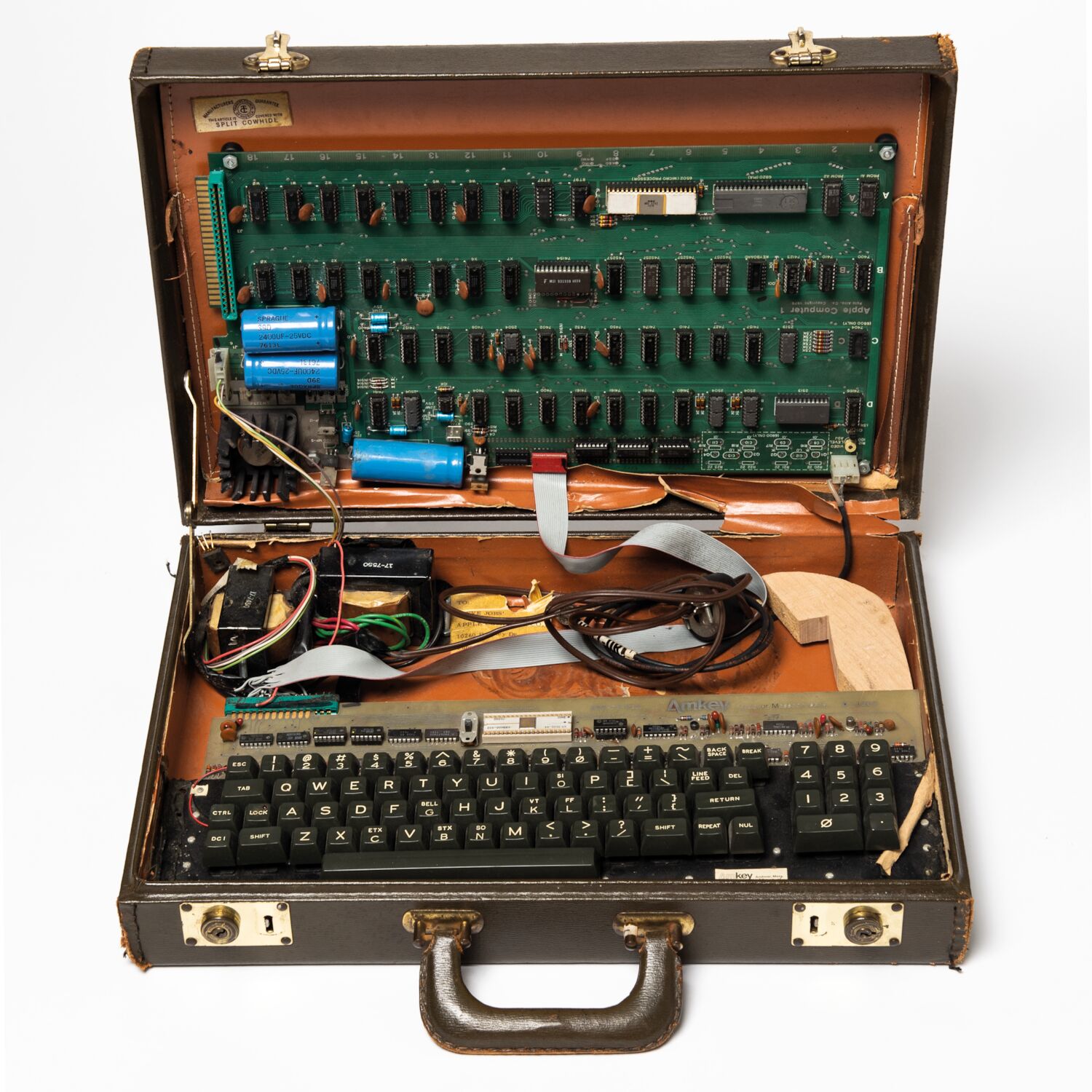 An open briefcase. The top half houses an Apple I circuit board, wired up to a keyboard in the bottom half.