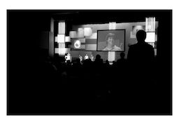 Viewed through a conference crowd, Steve - his clean-shaven, grinning face - is displayed on a large screen.