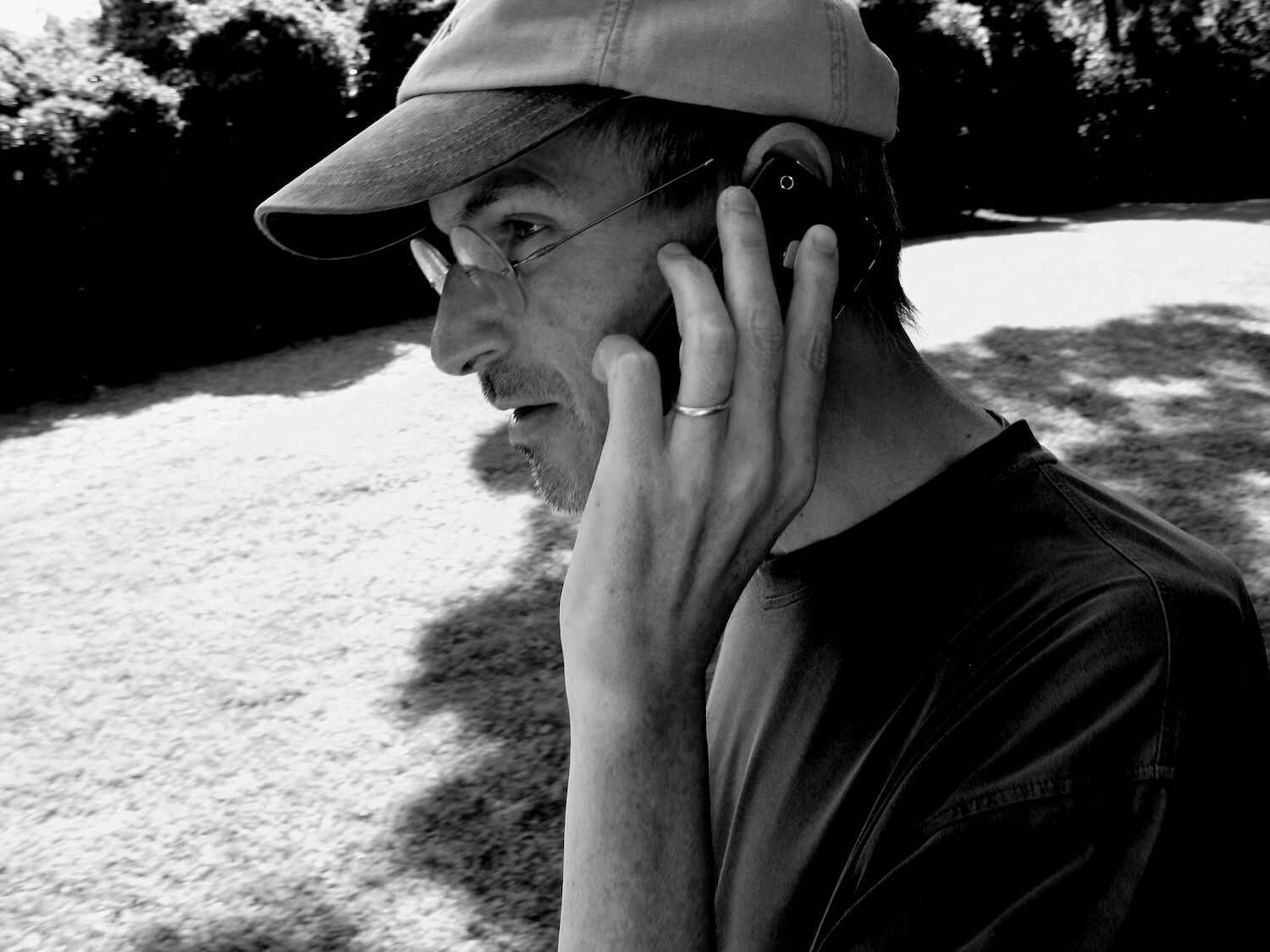 A candid photograph of Steve, wearing a baseball cap and black T-shirt, as he talks on his iPhone outdoors.