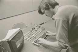 Steve hunches over a wooden desk, his hands on a keyboard hooked up to an Apple I circuit board.