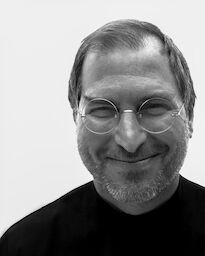Steve smiling, wearing his signature black turtleneck and round glasses.