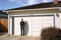 Steve stands against the white garage door of the house where Apple started in 1976. The house number reads 2066.