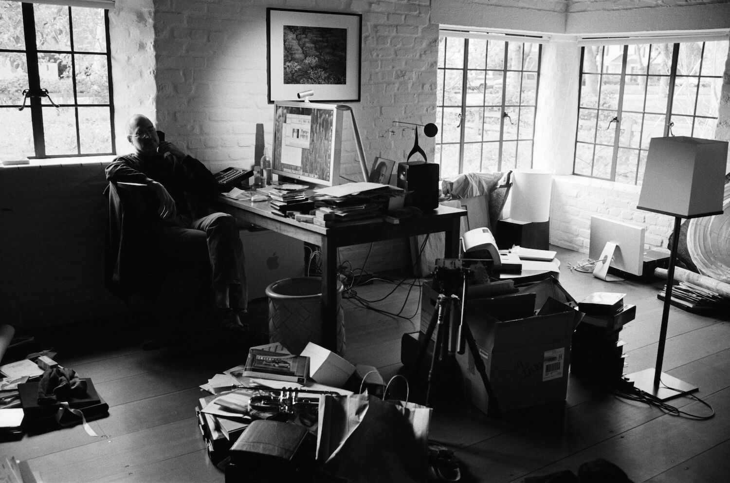 Steve sits cross-legged on the phone in his home office. The floor is strewn with boxes, papers, a tripod, and a trumpet.