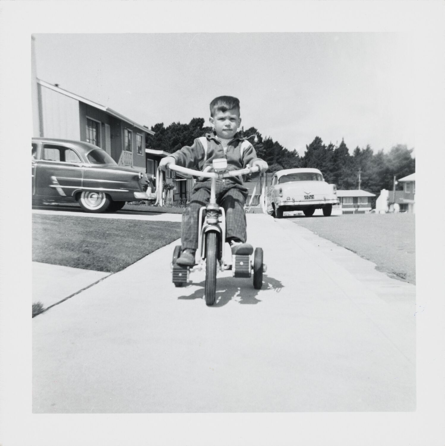 Two-year-old Steve rides a tricycle with tassels on the handlebars toward the camera.